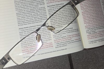 Reading glasses resting on an open Bible at Luke 9, magnifying the verses where James and John ask to call down fire