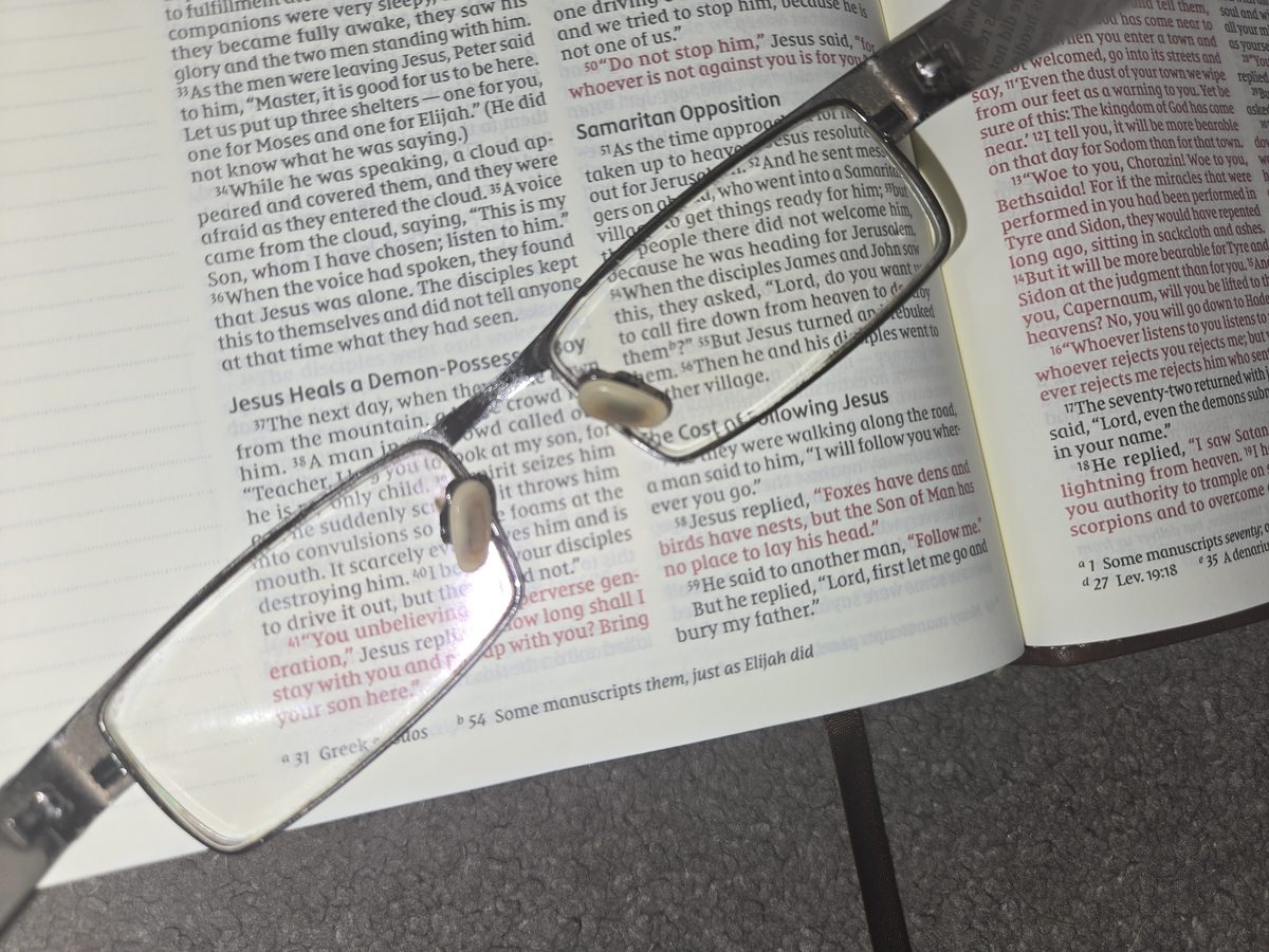 Reading glasses resting on an open Bible at Luke 9, magnifying the verses where James and John ask to call down fire